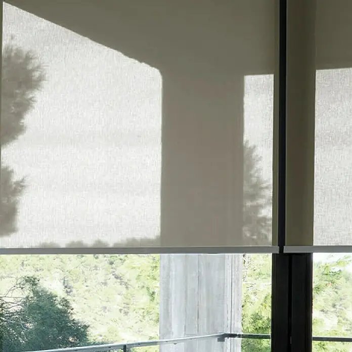 Estor enrollable screen 10% - An x Al: 120 x 250 cm, Perla lino - Primer plano de dos persianas enrollables beige, parcialmente bajadas y colgadas frente a ventanas con vistas a árboles verdes.