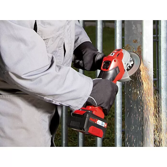 Einhell PXC 18V Amoladora angular de batería TE-AG 18/115 Li - 18 V, Sin batería, Diámetro disco: 115 mm, Con maletín - Amoladora angular inalámbrica roja y negra cortando un poste de metal oxidado, generando chispas.