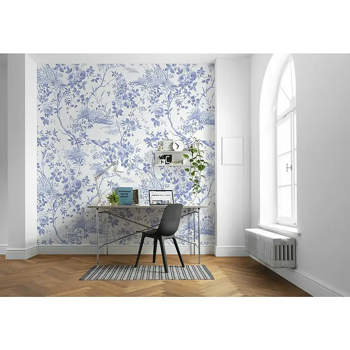 Komar Raw Fototapete Charming Bloom - 3 -tlg., B x H: 300 x 280 cm, Vlies - Ein Arbeitsbereich mit einem Schreibtisch, einem Stuhl, einer Lampe und einem Laptop vor einer floralen Tapete in Blau und Weiß.