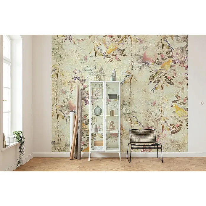Komar Raw Fototapete Cosy Bohemian - 3 -tlg., B x H: 300 x 280 cm, Vlies - Ein elegantes Wohnzimmer mit einer verzierten Tapete, die Vögel und Blumen darstellt, einem weißen Schrank und einem minimalistischen schwarzen Stuhl.