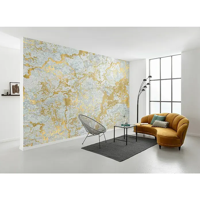Komar Raw Fototapete Marbelous - 8 -tlg., B x H: 400 x 280 cm, Vlies - Elegantes Wohnzimmer mit einer goldfarbenen Akzentwand, die dem Raum einen Hauch von Luxus verleiht. Ein modernes Sofa und ein stilvoller Sessel ergänzen das Design.