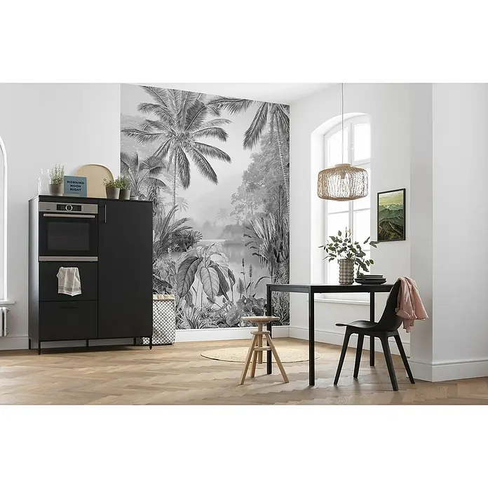 Komar Raw Fototapete Lac Tropical Black & White - 2 -tlg., B x H: 200 x 280 cm, Vlies - Schwarzer Küchenschrank mit eingebautem Ofen und Esstisch mit Stuhl in einem stilvollen Raum mit Dschungeltapete.