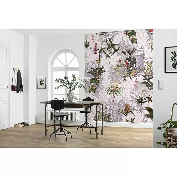 Komar Raw Fototapete Tropicana - 2 -tlg., B x H: 200 x 280 cm, Vlies - Botanische Tapete mit üppigen grünen Pflanzen, lila Mustern und rosa Vögeln auf hellrosa Hintergrund, an einer Wand in einem hellen Raum angebracht.