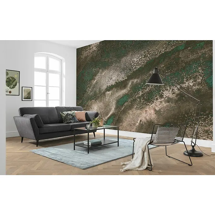 Komar Raw Fototapete Molten Copper - 8 -tlg., B x H: 400 x 280 cm, Vlies - Wohnzimmer mit dunkelgrauem Sofa, Couchtisch und modernem Sessel vor einer Wand mit abstraktem Muster.
