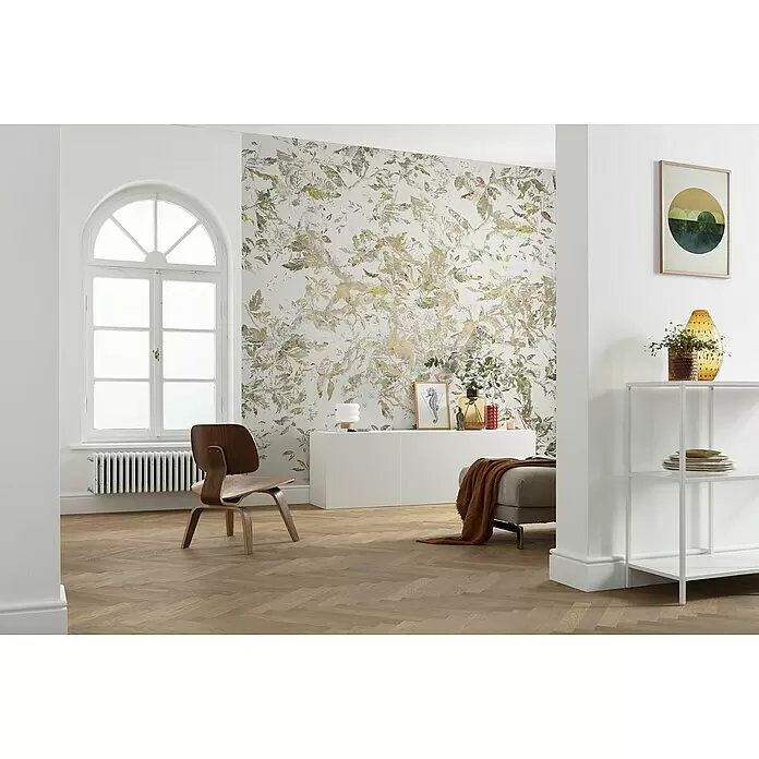 Komar Raw Fototapete Golden Feathers - 6 -tlg., B x H: 300 x 280 cm, Vlies - Botanische Tapete mit goldenen, grünen und rötlichen Blattmustern, die einen hellen Raum mit Holzfußboden und modernen Möbeln schmückt.