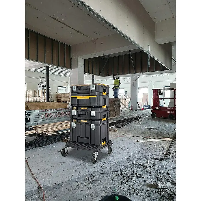DeWalt Werkzeugkasten TSTAK BOX IV - L x B x H: 333 x 440 x 302 mm, Kunststoff, Abschließbar - Werkzeugkoffer-Turm: Ein Stapel schwarzer Werkzeugkoffer mit gelben Akzenten auf einem Rollwagen in einer Baustelle.