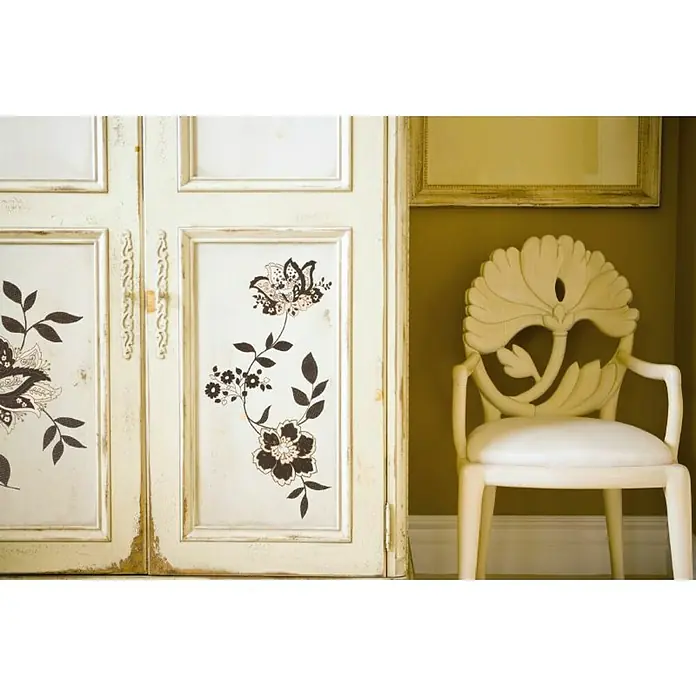 Komar Dekosticker Jackie - 4 -tlg., 70 x 50 cm - Nahaufnahme eines dekorierten Schranks in Cremeweiß mit floralem Design und einem passenden Stuhl mit blumenförmiger Rückenlehne daneben.