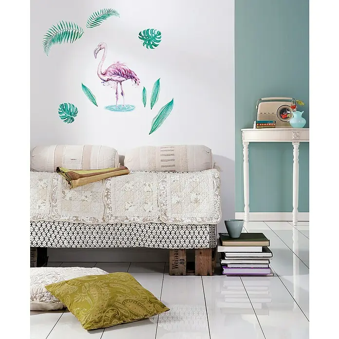 Komar Dekosticker Flamingo - 9 -tlg., 70 x 50 cm - Dieses Bild zeigt ein stilvolles Interieur mit einem Bett, das auf Paletten steht, dekoriert mit Kissen und einer Flamingo-Wanddekoration.
