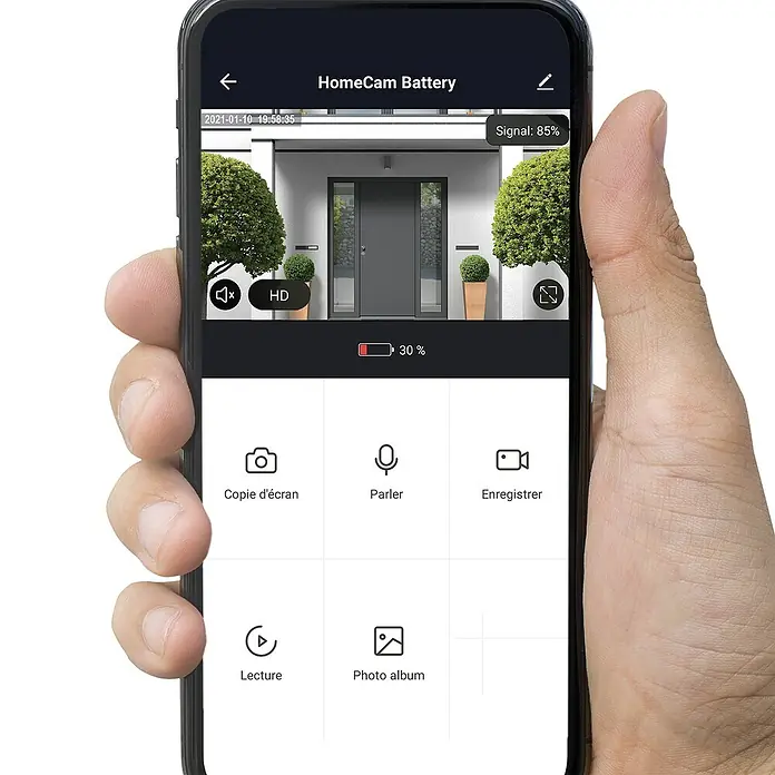 Überwachungskamera HomeCam Akku Outdoor - L x B x H: 55 x 50 x 90 mm - Smartphone mit der HomeCam Battery App, die eine Überwachungskamera mit 30% Akku und 85% Signalstärke anzeigt.