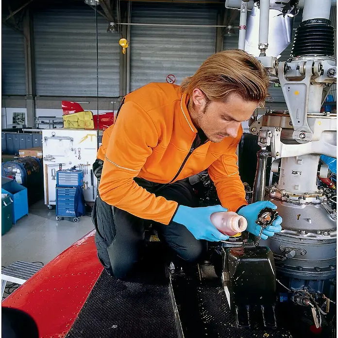 Einmalhandschuhe u-fit - XL, Kunststoff - Ein Mechaniker in orangefarbener Jacke füllt Öl in einen Motor. Blaue Handschuhe schützen seine Hände bei der Arbeit am Flugzeug.